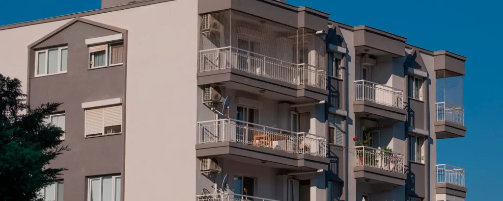Fachada de edificio residencial moderno de varios pisos con balcones, barandillas blancas y aire acondicionado.